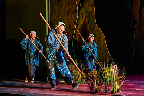 Members of the My Neighbour Totoro company puppet reeds with long wooden sticks. They wear outfits in shades of blue with headscarves.