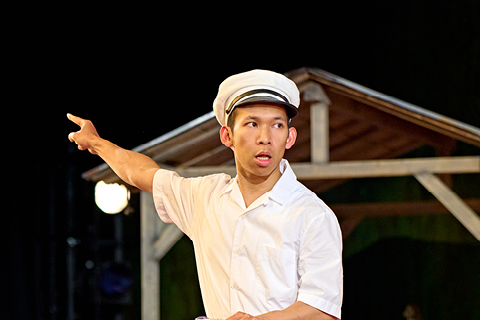 Kanta (Ka Long Kelvin Chan) wears a white shirt, blue shorts, a blue hat and blue and white pumps and holds a wooden basket.